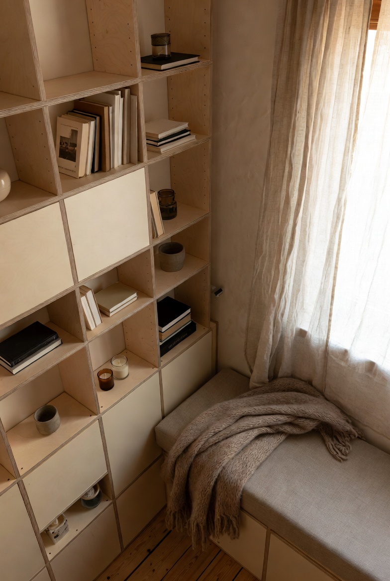 A neutral reading nook window seat framed by birch plywood book shelves
