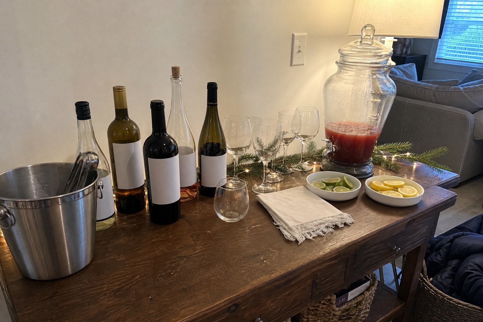A holiday hosting drink station with glassware, mugs, greenery and warm string lights