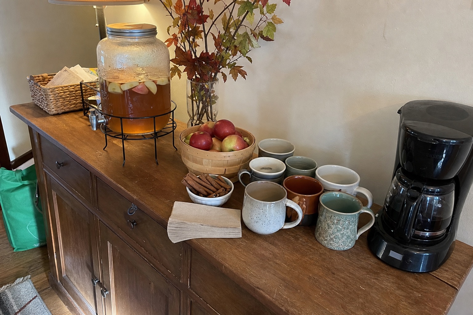 A Thanksgiving cider and coffee station with mugs, glassware, cinnamon and a clear serving area